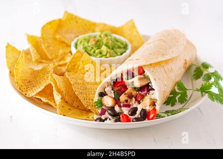 Burrito de poulet et de haricots noirs sur une assiette blanche avec des chips de tortilla de maïs et du guacamole Banque D'Images