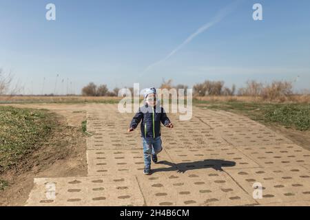 Petit garçon dans des lunettes de soleil courant le long de la colline et souriant Banque D'Images