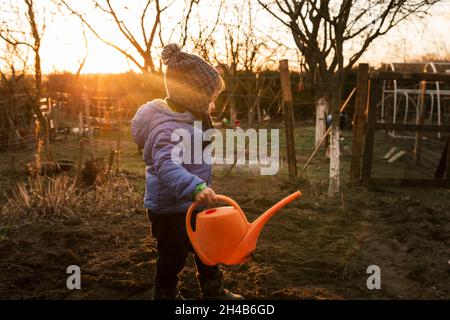 Un tout-petit garçon arrose des plantes fraîchement plantées avec de l'eau à l'orange Banque D'Images