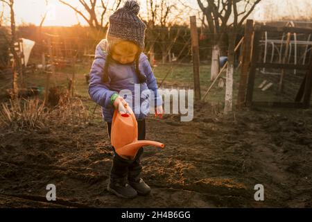 Un tout-petit garçon arrose des plantes fraîchement plantées avec de l'eau à l'orange Banque D'Images