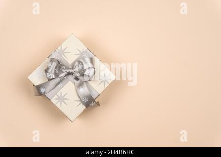 Boîte cadeau de Noël avec ruban argenté et noeud sur un fond délicat avec un endroit pour l'inscription des voeux.Heure de Noël.Copier l'espace Banque D'Images