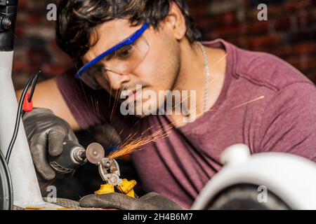 Un mécanicien spécialisé portant des lunettes de sécurité à l'aide d'une mini meuleuse pour couper une vis dans la réparation d'un scooter électrique. Banque D'Images