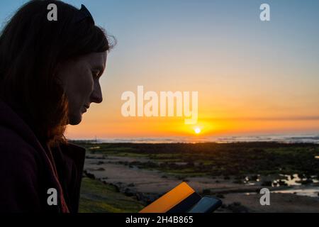 Femme utilisant un téléphone portable pendant que le soleil se couche à West Runton Beach Banque D'Images