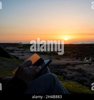 Femme utilisant un téléphone portable pendant que le soleil se couche à West Runton Beach Banque D'Images
