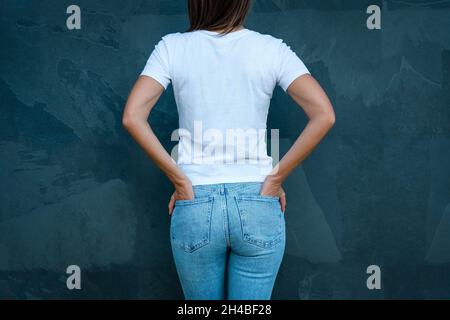 T-shirt mousselé blanc pour un motif imprimé.Vue arrière ou vue arrière d'une femme en t-shirt blanc vierge et Jean bleu sur fond gris Banque D'Images