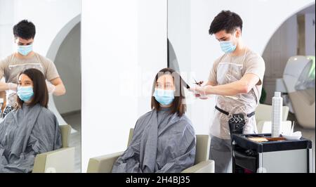 Femme cliente en masque pendant les coupes de cheveux au salon de beauté Banque D'Images