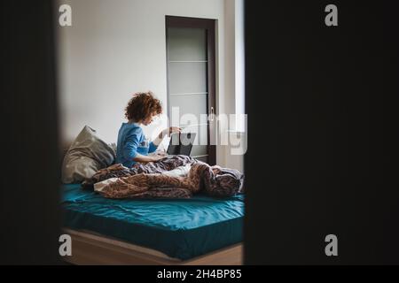 Jeune femme passant la matinée à surfer sur Internet.Vue de la porte à moitié ouverte Banque D'Images