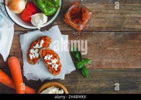 Pain complet recouvert de sauce tomate-poivre et de fromage feta sur une ancienne table rustique en bois.Plat de légumes bio fait maison. Banque D'Images