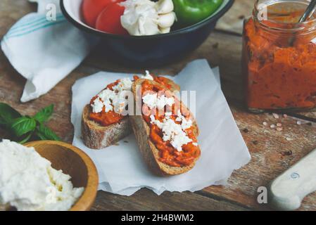 Pain complet recouvert de sauce tomate-poivre et de fromage feta sur une ancienne table rustique en bois.Plat de légumes bio fait maison. Banque D'Images