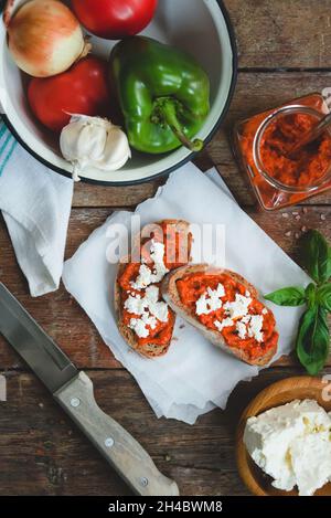 Pain complet recouvert de sauce tomate-poivre et de fromage feta sur une ancienne table rustique en bois.Plat de légumes bio fait maison. Banque D'Images