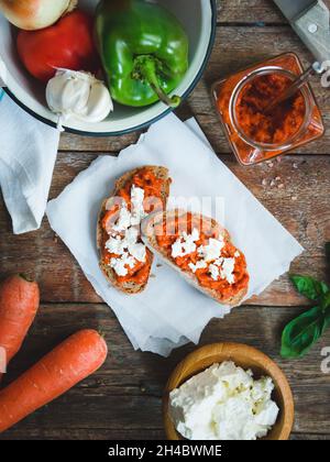 Pain complet recouvert de sauce tomate-poivre et de fromage feta sur une ancienne table rustique en bois.Plat de légumes bio fait maison. Banque D'Images