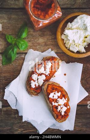 Pain complet recouvert de sauce tomate-poivre et de fromage feta sur une ancienne table rustique en bois.Plat de légumes bio fait maison. Banque D'Images