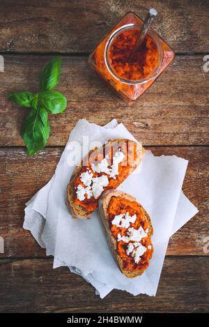 Pain complet recouvert de sauce tomate-poivre et de fromage feta sur une ancienne table rustique en bois.Plat de légumes bio fait maison. Banque D'Images