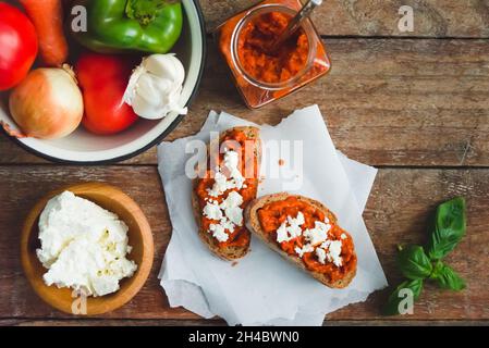 Pain complet recouvert de sauce tomate-poivre et de fromage feta sur une ancienne table rustique en bois.Plat de légumes bio fait maison. Banque D'Images