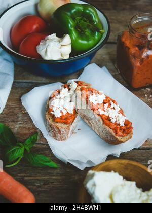 Pain complet recouvert de sauce tomate-poivre et de fromage feta sur une ancienne table rustique en bois.Plat de légumes bio fait maison. Banque D'Images