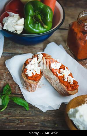 Pain complet recouvert de sauce tomate-poivre et de fromage feta sur une ancienne table rustique en bois.Plat de légumes bio fait maison. Banque D'Images