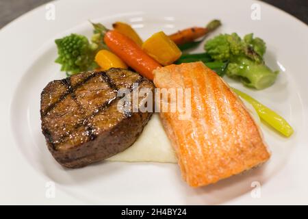 Une assiette à dîner avec steak, saumon grillé, purée de pommes de terre et légumes rôtis est en cours de préparation. Banque D'Images