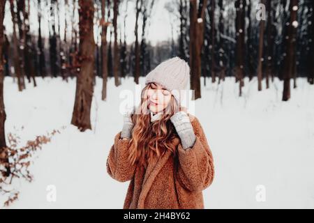 Photo de jeune belle femme en fourrure debout sur la neige blanche en forêt d'hiver.La fille est souriante et heureuse avec les yeux fermés.La femme a l'hiver Banque D'Images