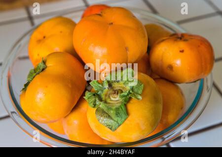 Un bol rempli de persimmons se trouve sur un comptoir de cuisine. Banque D'Images