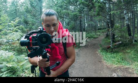 Vidéaste professionnel tenant un appareil photo reflex numérique sur un dispositif de stabilisation de nacelle 3 axes dans la forêt.Directeur de la photographie.Ralenti Banque D'Images