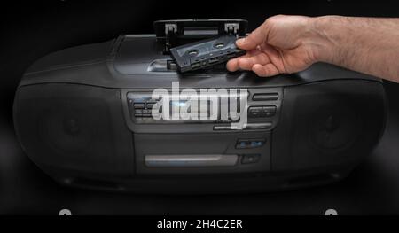 man place une cassette dans un magnétophone sur fond noir Banque D'Images