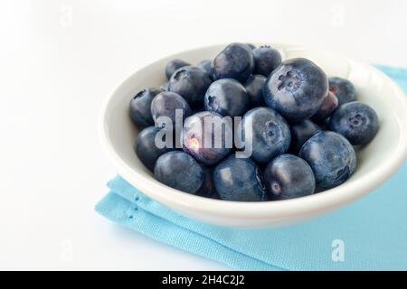 Gros plan des bleuets dans un bol en porcelaine blanche avec une serviette bleue isolée sur du blanc.Faible profondeur de champ.Mise au point sélective. Banque D'Images