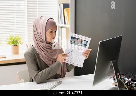 Professeur d'économie confiant pointant vers le document financier tout en étant assis devant l'écran d'ordinateur et en expliquant le sujet au public en ligne Banque D'Images