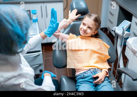 Dentiste amical donnant élevé cinq petite fille patient assis sur une chaise dentaire après l'examen Banque D'Images