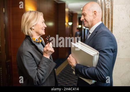 Deux collègues élégants et matures discutent de nouvelles ou de points de travail dans un couloir de bureau contemporain Banque D'Images