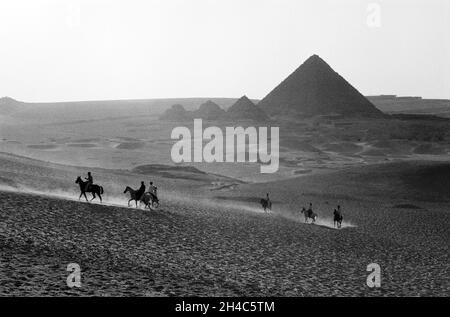 Afrique, Égypte, Giza, 1976. Cavaliers dans le désert avec la pyramide de Menkaure et les trois plus petites pyramides des Queens. Banque D'Images