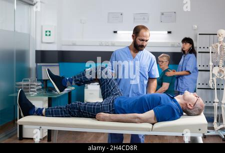 Homme avec une lésion musculaire de jambe recevant un massage orthopédique pour la physiothérapie.Infirmière aidant le patient à la retraite avec des douleurs au genou, soulageant la pression pour la récupération physique et la kinétothérapie. Banque D'Images