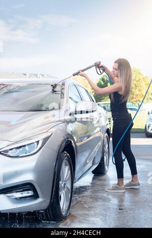 Jolie femme blonde en Jean et t-shirt noir lavant la voiture Banque D'Images