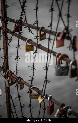 VERONA, ITALIE - 09 juin 2019 : un cliché vertical de cadenas enfermés sur une porte en métal avec un fil barbelé et des messages d'amour sur les écluses avec de l'eau dans le Banque D'Images