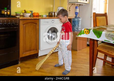 un petit garçon balaie le sol de la cuisine avec un balai Banque D'Images