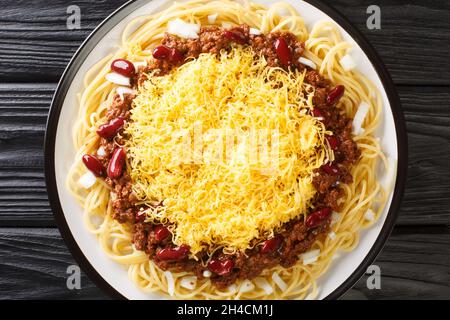 Spaghetti au Chili de Cincinnati maison avec haricots rouges et oignon gros plan dans l'assiette sur fond de bois noir.Vue horizontale du dessus de abo Banque D'Images