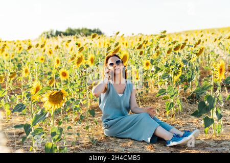 jeune femme adulte parlant sur le smartphone assis dans un champ de tournesols Banque D'Images