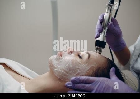 Jeune femme recevant un massage facial de levage RF électrique au spa de beauté avec équipement d'électroporation dans la clinique Banque D'Images