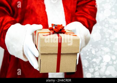 Le Père noël a des mains gantées tenant une boîte cadeau avec un ruban rouge. Banque D'Images