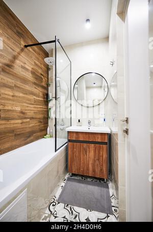 Salle de bains lumineuse avec mobilier en bois, miroir rond et belle baignoire de couleur blanche.Concept de salle de bain élégante et moderne avec une bonne lumière. Banque D'Images