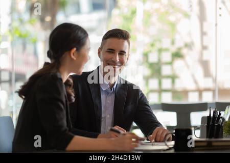 Un mentor multiethnique de race blanche et une femme asiatique assis à un bureau avec un ordinateur portable font de la paperasserie en discutant ensemble du rapport financier du projet.Entreprise Banque D'Images