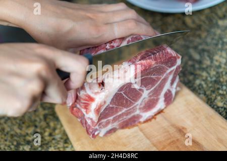 Les mains des femmes ont coupé gros plan avec un couteau un grand morceau de viande de porc fraîche sur une planche à découper, espace de copie, vue du dessus Banque D'Images