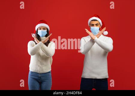 Arrêter la propagation du coronavirus, garder la distance sociale.Jeune couple arabe en masque de protection et chapeau de père Noël croisant les mains Banque D'Images