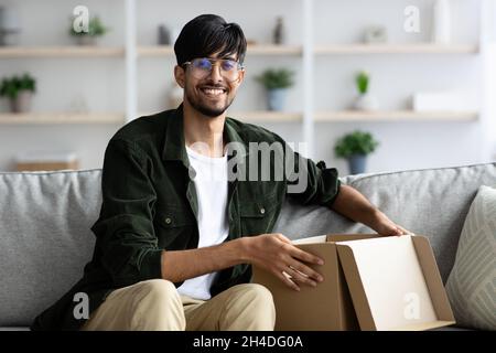 Un homme arabe souriant ouvre une boîte en papier, intérieur de la maison Banque D'Images