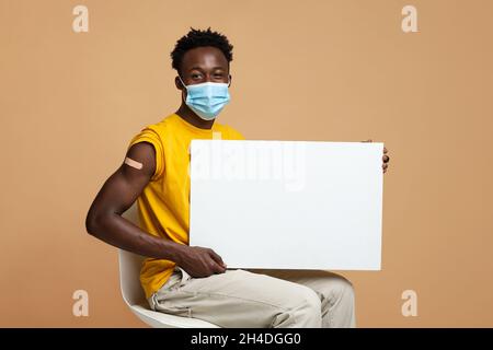 Black Guy vacciné dans masque médical protecteur tenant blanc Placerard Banque D'Images