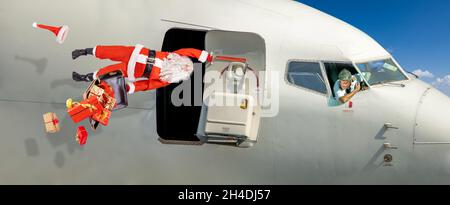 Un Père Noël choqué avec des cadeaux dans une valise tenant une poignée dans la porte ouverte d'un avion volant Banque D'Images