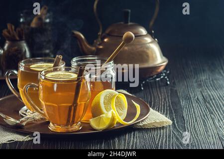 Thé épicé aux toddies chaudes ou au citron avec théière en cuivre et ingrédients sur plateau dans une ferme rustique sombre Banque D'Images