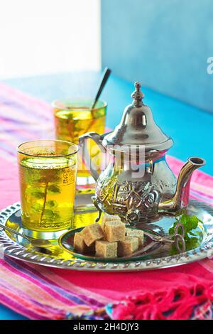 Deux verres de thé chaud à la menthe marocaine sur un plateau métallique avec un thé, de la menthe et des cubes de sucre brun Banque D'Images