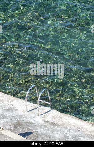 Plan vertical d'une échelle métallique menant à une piscine d'eau de mer claire Banque D'Images