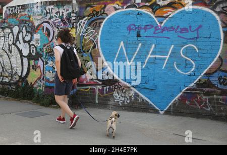 Une femme passe un chien devant un graffiti rendant hommage aux travailleurs du NHS dans l'est de Londres, alors que le Royaume-Uni continue de se maintenir en isolement pour aider à freiner la propagation du coronavirus.Date de la photo: Vendredi 24 avril 2020. Banque D'Images