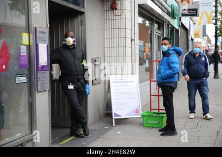 Des personnes portant des équipements personnels de protection font la queue devant une succursale de NatWest Bank à East Ham, dans l'est de Londres, alors que le Royaume-Uni continue de se verrouiller pour aider à freiner la propagation du coronavirus.Date de la photo: Mardi 28 avril 2020. Banque D'Images